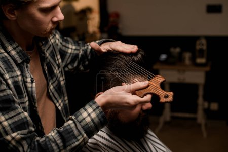 Photo for Male barber accurate doing hair styling to a male client with an afropic comb with long metal teeth - Royalty Free Image
