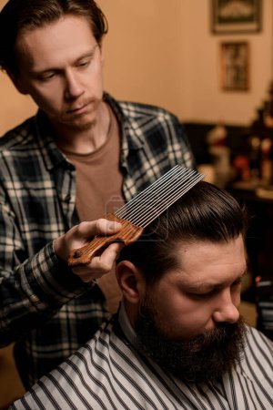 Photo for Male barber masterfully doing hair styling to a male client with an afropic comb with long metal teeth - Royalty Free Image