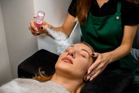 close-up of female client and beautician carefully moisturizes her face with steam from portable humidifier. Beauty treatment of face in beauty center