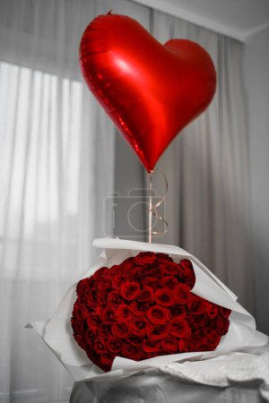 Foto de Amplio ramo de rosas rojas y globo de aire en forma de corazón sobre un fondo claro y borroso. Sorpresa para la persona más amada - Imagen libre de derechos