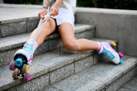 Téléchargez les photos : Portrait recadré de jambes en patins à roulettes vintage colorés chaussures isolées sur fond de rue. Fille attache lacets sur rouleaux - en image libre de droit