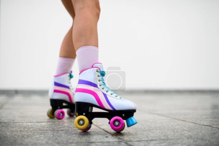 Téléchargez les photos : Photo recadrée de jambes féminines en patins à roulettes vintage colorés chaussures isolées sur fond de mur blanc. concept d'équilibre extrême, rue en dehors du mode de vie urbain - en image libre de droit