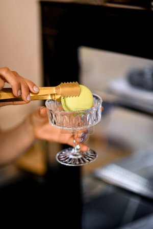 Téléchargez les photos : Femme utilisant des pinces pour mettre le macaron dans un vase transparent à l'ancienne pour les desserts, mise au point sélective. Serveuse au service des clients commande, gros plan - en image libre de droit
