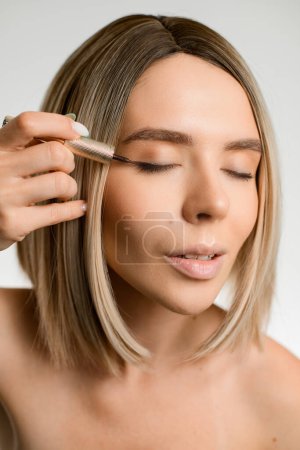 Photo for Young beautiful blonde woman with bare shoulders using contour brush while drawing arrows on eyelids, closed eyes - Royalty Free Image