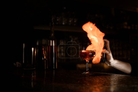 Foto de La mano de camarera femenina prepara cóctel de fuego con spray y cerillas encendidas en el mostrador de la barra junto a botellas y otros accesorios de camarero - Imagen libre de derechos