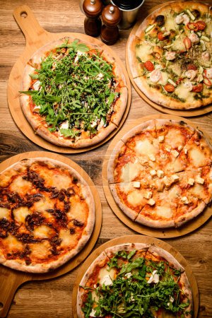 Téléchargez les photos : Cette vue de dessus captivante présente un ensemble de cinq pizzas, magnifiquement éclairées pour mettre en évidence leurs détails et saveurs délicieux. - en image libre de droit