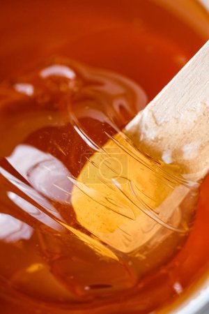 Leuchtend gelbe transparente Zuckerpaste oder Wachshonig in einem Behälter mit einem dünnen Holzspatel