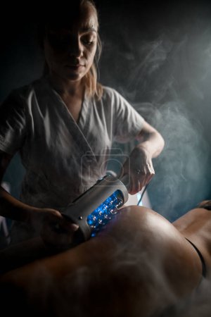 Photo for Cosmetologist performs an anti-cellulite massage on a woman in underwear with a beautiful body using an endomassage device with illumination - Royalty Free Image