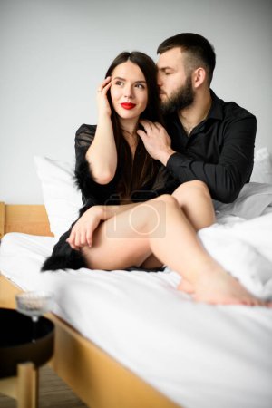 Téléchargez les photos : Amour d'un homme et d'une femme le jour de la Saint-Valentin. Amoureux assis ensemble sur un grand lit en bois az femme bien-aimée et homme bien-aimé. - en image libre de droit