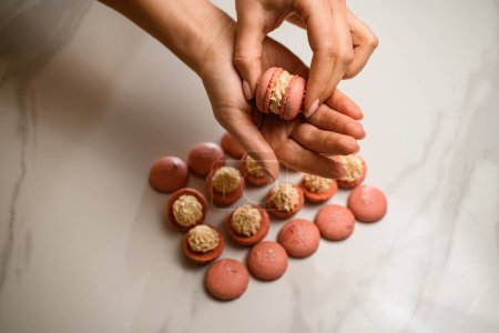 Voyage visuel à travers le processus étape par étape de création de macarons beiges, soulignant l'ajout d'un remplissage crémeux.