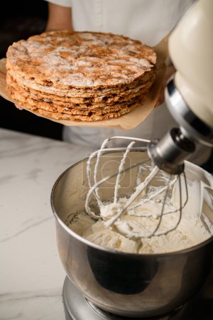 pastry chef adds a finishing touch, carefully layering whipped cream on a delightful cake.