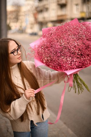 Enorme ramo de flores rústicas de gypsophila en color rosa florista niña sosteniendo en las manos. Vista frontal. Fondo de calle borrosa