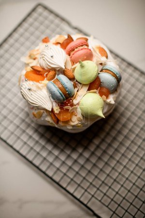 Beautiful and tasty Easter cake decorated with white icing, colorful beret macaroons of different shapes and other confectionery decor