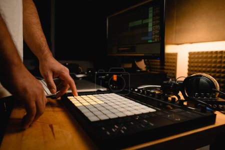 Close-up of a copper controller on a wooden desktop, male hands pressing white keys on it. On the blurred background is other professional recording studio equipment