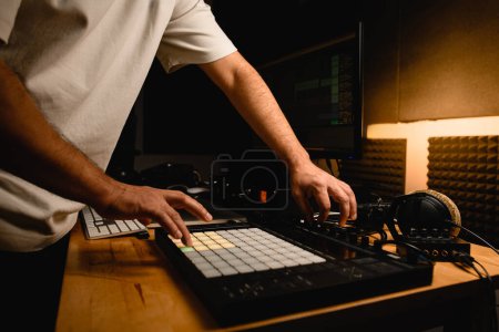 Close-up side view of midi controller on desktop, male hands pressing keys on it. Nearby is other professional sound recording equipment