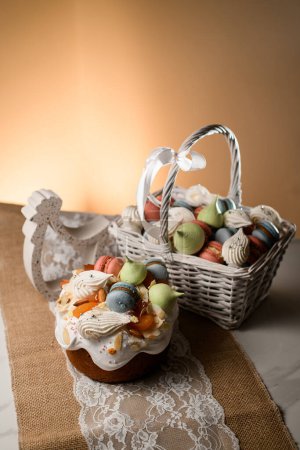 Téléchargez les photos : Beau gâteau de Pâques décoré avec un panier rempli de macarons et meringue et un coq décoratif sur une serviette en dentelle blanche - en image libre de droit