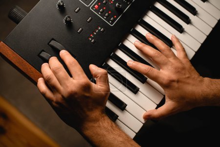 músico presionando las teclas de un sintetizador profesional con una mano y girando los controles del equipo con la otra mano en un estudio de grabación