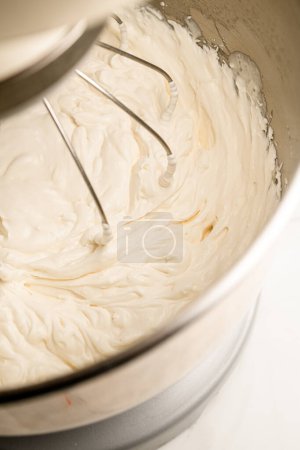 Whipping white cream in a standard electric mixer with a whisk attachment standing on a white kitchen table