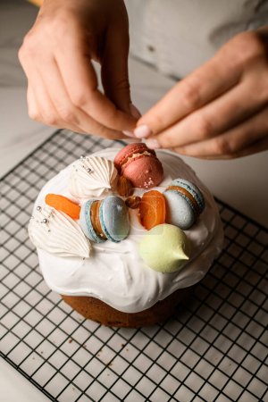 Bäcker dekorieren Osterkuchen mit weißer Glasur bunte Makronen, getrocknete Aprikosen und Baiser in verschiedenen Formen