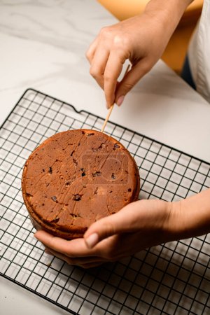 Woman checks with a wooden skewer the readiness of the Easter cake, which is lying on a metal grid