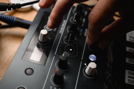 Close up top view of male hand turning two fingers knob on music recording controller in recording studio, focus on foreground
