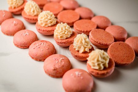 Demi-blancs roses pour un beau dessert macaron français à la crème sur une table de cuisine blanche, biscuits en forme de sandwich