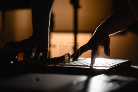 Side view of male hands pressing keys on copper controller in low light in recording studio