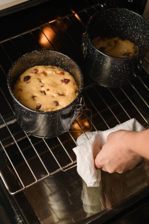 Bäcker holt mit einem weißen Handtuch zwei Osterkuchen in Metallformen aus dem Ofen, die auf einem Gestell stehen