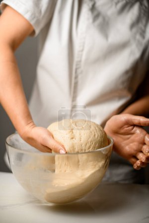Master chef in white clothes prepares the dough for the production of sweets in a deep glass bowl