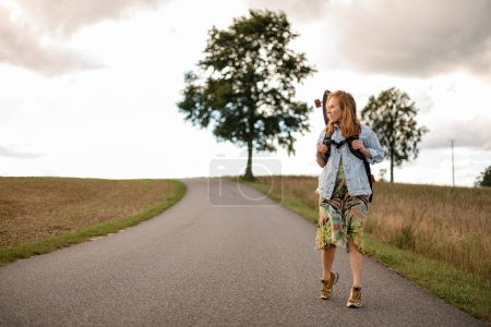 Casual and carefree, she walks along the road, a longboard resting on her back.