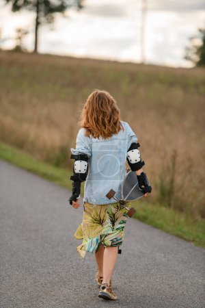peaceful country road stretches ahead as the girl, longboard in tow, moves forward, creating a calming rear view.