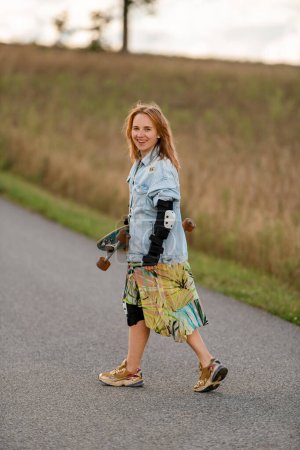 With a cheerful smile, she turns around, longboard in hand, embracing the scenic country road ahead.