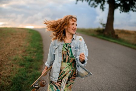 On a country road, she effortlessly showcases style in a light blue denim jacket with a longboard.