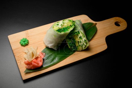 Enjoy the crisp freshness of a spring roll filled with cucumber and avocado, elegantly presented on a banana leaf with a side of ginger and wasabi.