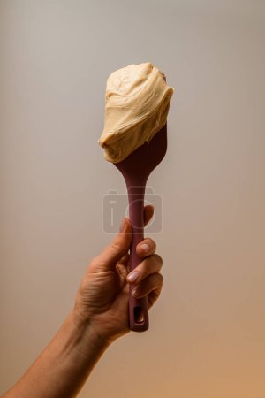Pastry chef hand holding natural light beige whipped cream Photo of light cream on a light background