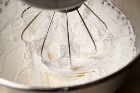 Using a mixer, whipping thick white cream from egg whites and sugar to decorate a appetizing macaroons