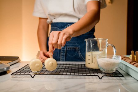 Hands of culinary making a delicious macaron in white soft chocolate on a beige background. Chocolate-covered macaroon