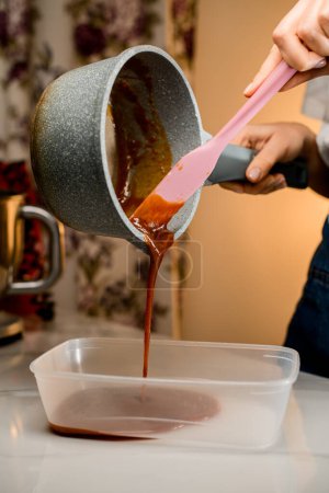 Poring crème brune épaisse pour la décoration de macarons à l'aide d'une spatule silicone rose doux