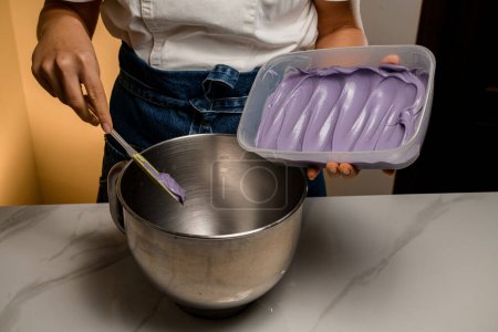 Metal bowl and delicious lavender cream in plastic container on a marble table. Woman in blue jeans and a white top