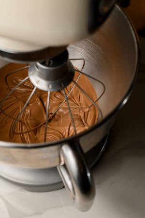 Mit einem Mixer schlägt man dicke hellbraune Sahne aus Eiweiß und Zucker, um einen Makronenkuchen zu dekorieren