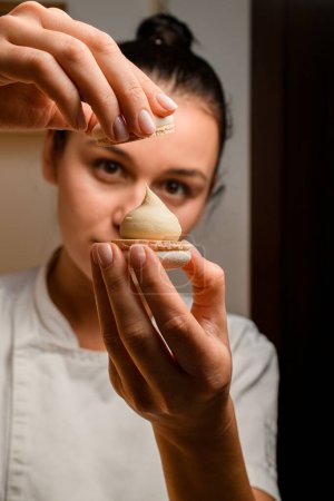 Macht köstlichen Macaron mit geschickten Händen von Spezialisten in einem weißen Top mit hellbrauner zarter Creme