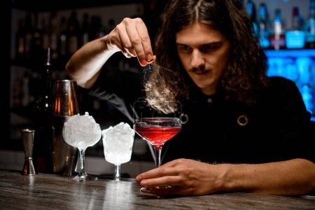 Bartender squeezes a piece of zest, holding it directly above the cocktail glass so that the splashes fly into the cocktail, and carefully observes the process