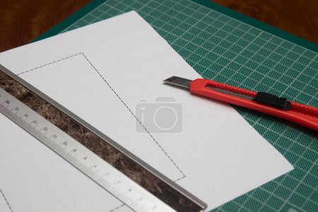 Photo for Someone cutting a paper with the help of a cutter and a ruler on a green work table - Royalty Free Image