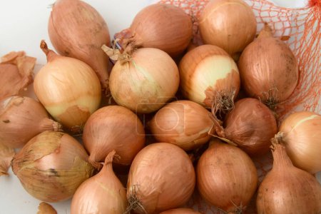 Photo for Close-up of some small raw unpeeled onions next to the container on a white surface viewed from above - Royalty Free Image