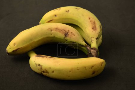 Téléchargez les photos : Une main de bananes des îles Canaries (Espagne) avec de petites taches qui marquent leur état de maturité sur un fond noir - en image libre de droit