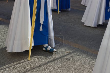 Téléchargez les photos : Détail des pieds de certains Nazaréens avec des sandales bleues et une tunique blanche dans une procession du dimanche des Rameaux en Espagne - en image libre de droit