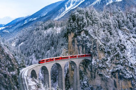 Foto de Vista aérea del Tren pasando por la famosa montaña de Filisur, Suiza. Landwasser Viaducto Patrimonio de la Humanidad con tren expreso en los Alpes suizos nieve invierno paisaje. - Imagen libre de derechos