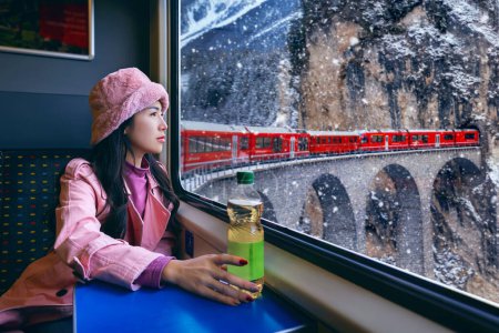 Téléchargez les photos : Touriste regardant par la fenêtre profiter avec Train passant par la célèbre montagne à Filisur, en Suisse. Landwasser Viaduc patrimoine mondial avec train express dans les Alpes suisses neige paysages d'hiver. - en image libre de droit