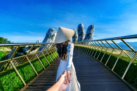Turista mujer sosteniendo la mano del hombre y llevándolo al puente de oro en Da Nang, Vietnam.