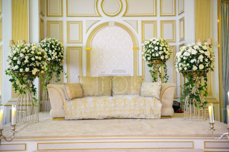 Una boda tradicional de estilo marroquí elegantemente escenificada con un gran sofá para que la pareja se siente y reciba bendiciones de los invitados, rodeada de hermosas decoraciones florales y candelabros
